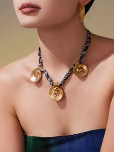 Close-up of golden spiral disc pendants on a chic black and white woven cord necklace