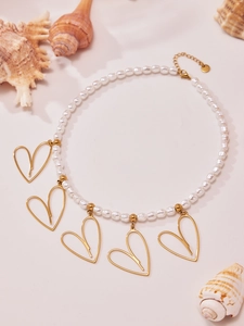 Dettaglio della collana di perle con cinque ciondoli a cuore dorati su sfondo sabbia beige