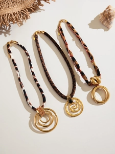 Three animal print fabric necklaces with bold gold pendants on a minimalist cream background