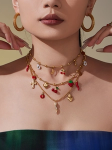 Detail of layered gold necklace with enamel chili, cherry, and ladybug pendants