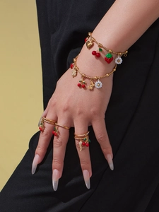 Detail of gold layered bracelet and rings with colorful enamel fruit and bee charms