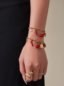 Détail de bracelets à breloques dorés avec pendentifs cerise et fraise sur main de mannequin
