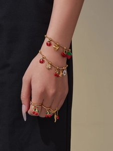 Detail view of gold jewelry set featuring enamel ladybug and cherry charms on bracelets