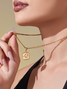Dettaglio di una collana d'oro con ciondolo floreale quadrato indossata da una modella