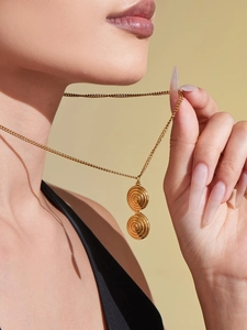Close-up of a double spiral pendant on a gold chain necklace worn by a fashion model