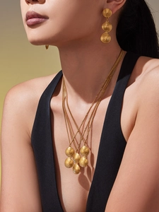 Detail of layered gold-plated spiral disc necklaces and matching drop earrings on model