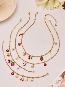 Detail of gold beaded chains with enamel strawberry and ladybug pendants on ceramics