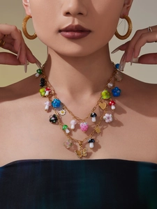 Detail of layered gold necklace with mushroom, strawberry, and butterfly pendants