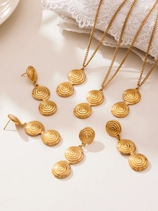 Detail of gold spiral disc necklace and earring set on white lace and fabric background