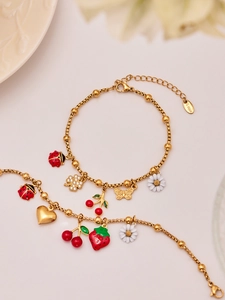 Detail showing colorful enamel pendants like cherry and ladybug on a gold box chain bracelet