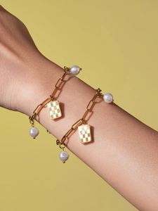 Close-up of golden paperclip chain bracelet with white pearls and checkered charm