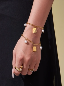 Golden chain bracelet with pearl and checkerboard charms worn with a leopard ring