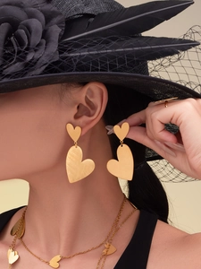 Detail of gold heart earrings with brushed metal finish on model in a jewelry set