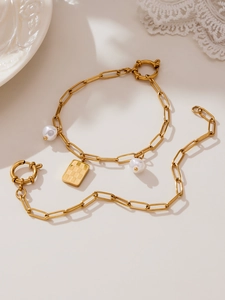 Detail of gold chain set with white pearl charms and a rectangular textured pendant