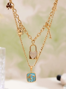 Dettaglio della collana dorata a strati con lucchetto a cuore e ciondolo blu fiorito