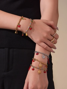 Close-up of gold beaded bracelets with strawberry and sun enamel charms and rings