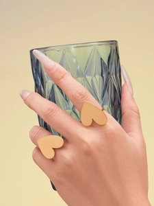 Macro shot of gold heart rings worn on a hand holding a blue glass for a luxury look