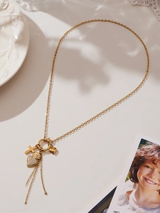 Detailansicht der goldene Quastenhalskette mit Kreuz und Herzanhängern auf Vintage-Teller