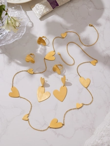 Detailed view of gold heart jewelry set with brushed finish on white marble surface
