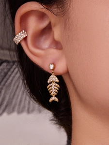 Détail des boucles d'oreilles arêtes de poisson dorées avec zircons sur l'oreille