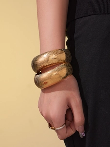 Dettaglio macro di bracciali dorati con texture a pelle di serpente e spazzolata al polso
