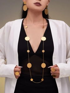 Detailweergave van lange gouden ketting met schijfjes en bijpassende sieraden op model
