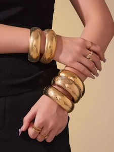 Dettaglio di bracciali rigidi placcati in oro 18k con finiture martellate e a nido d'ape