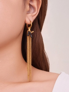 Dettaglio di orecchini dorati a frangia con corallo nero e nappe di perline su modella