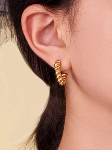 Macro shot of gold-plated croissant-style twisted rope earrings worn on earlobe