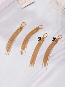 Dettaglio di orecchini a frangia placcati oro 18k con accenti neri e bianchi su seta