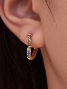 Detail of 18k gold huggie earrings with peacock blue gradient zircons on ear