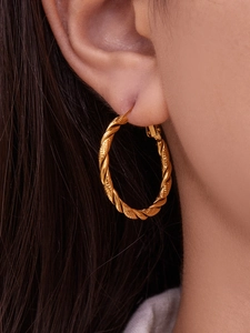 Dettaglio ravvicinato di orecchini a cerchio intrecciati placcati oro 18k indossati da modella