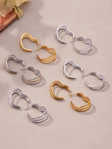Macro detail of triple-layered 18k gold heart-shaped earrings on elegant texture