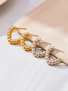 Detailed close-up of gold and silver twisted hoop earrings on a beige suede jewelry pouch