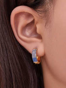 Close-up of gold huggie hoop earrings with gradient blue zircon crystals on ear