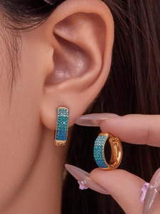 Detail of gold hoop earrings with gradient blue zircon inlay worn on the ear