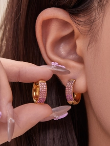 Detail of gold hoop earrings with gradient pink and purple zircons worn on the ear