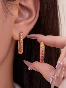 Close-up of gold U-shaped hoop earrings with pink cubic zirconia on ear and hand