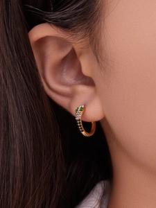 Macro shot of 18k gold snake hoop earrings with green zircon eyes and gradient stone pavé