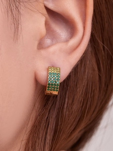 Gros plan de boucles d'oreilles créoles dorées avec cristaux verts dégradés
