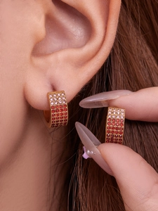 Vue détaillée des boucles d'oreilles huggie dorées avec zircons roses et rouges dégradés