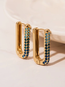Macro shot of U-shaped gold earrings with gradient blue zircon stones on ceramic base