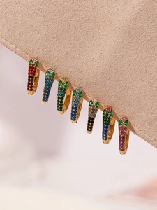 Macro view of gold snake-shaped hoop earrings with colorful zircon stones on suede
