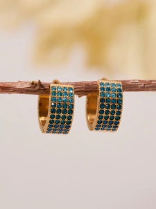 Détail de boucles d'oreilles créoles dorées 18k avec zircons bleus sur bois