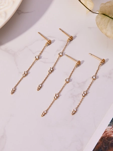 Détail de boucles d'oreilles pampilles dorées avec zircone sur marbre blanc