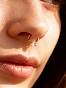 Detail of gold titanium septum ring featuring a pear-cut zircon in a 3-prong setting