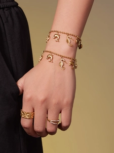 Detail van vergulde armbanden met dolfijnbedels en zonnebloemring gedragen door een model