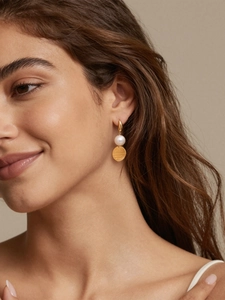 Détail des boucles d'oreilles dorées 18 carats avec perle et pendentif sur un mannequin