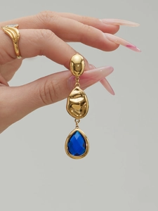 Detail of long teardrop earrings with blue faceted stone and gold-plated metal texture
