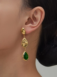 Close-up of golden tiered earrings with green teardrop stones on a fashion model